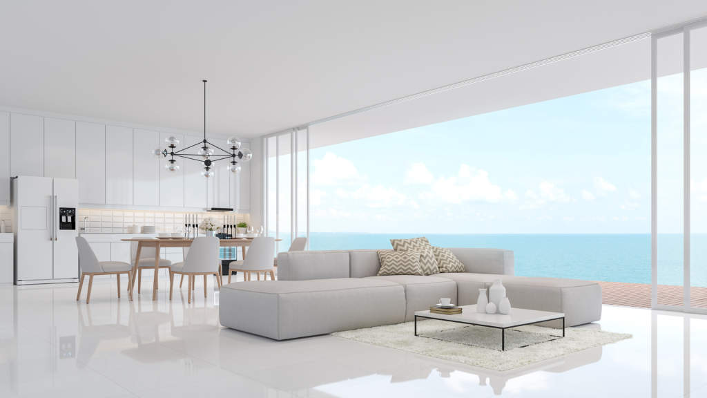Open plan living room with a white sofa and floor to ceiling windows overlooking the blue ocean.